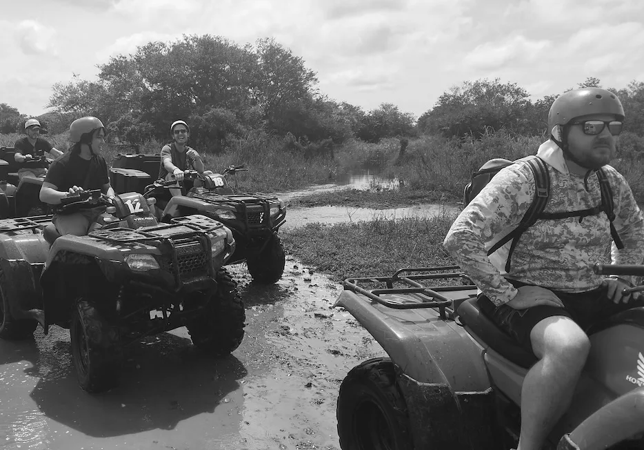 Teammates riding ATVs through the mud.
